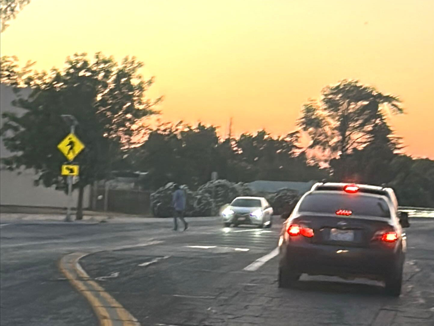 Pedestrian in crosswalk in low light in front of cars along Yosemite.
