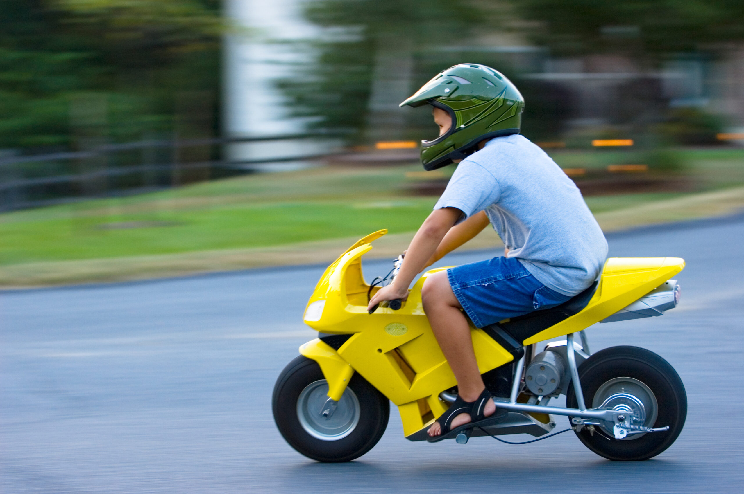 Child with helmet on riding yellow minibike. Riding on paved surface.
