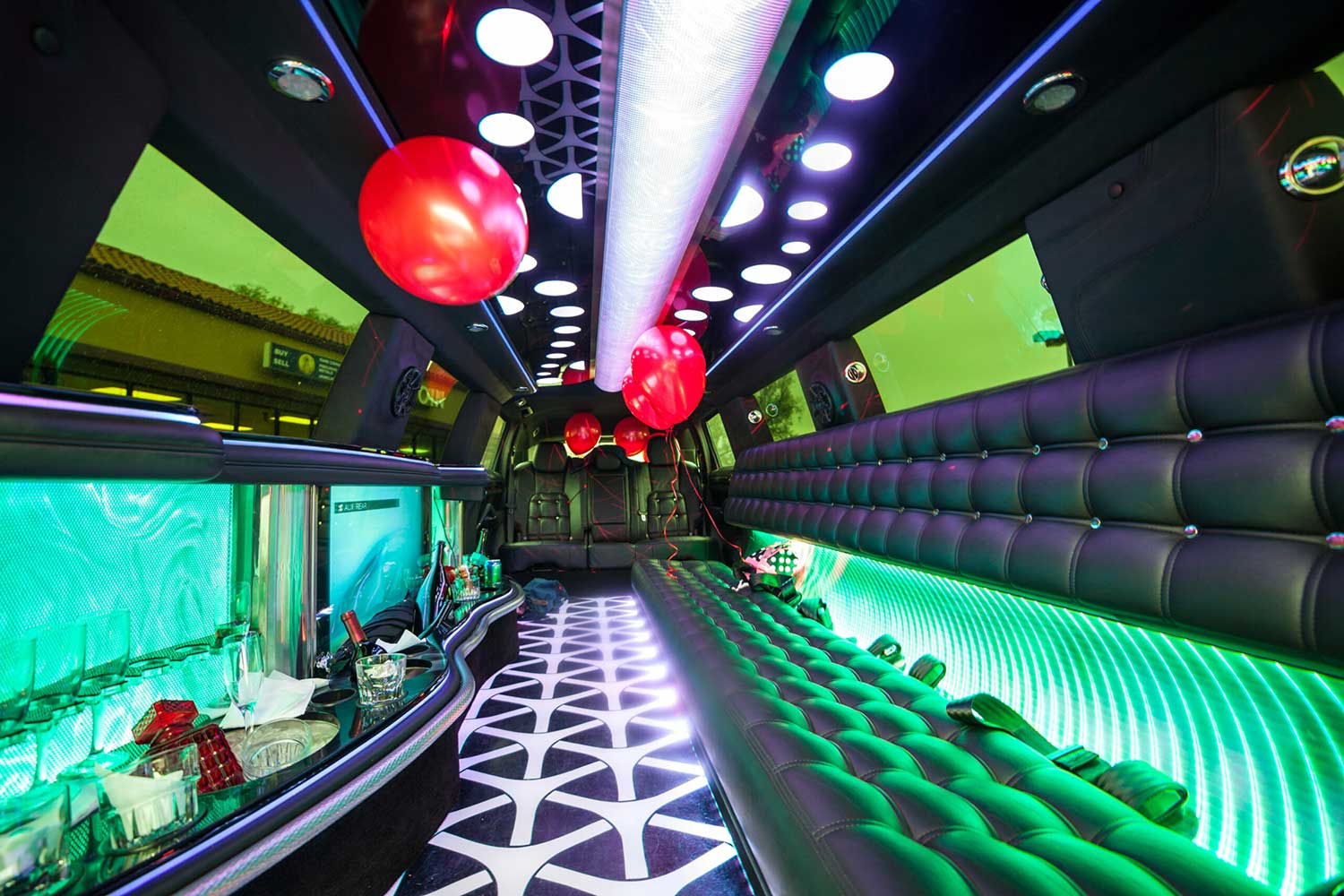Red balloons in the cabin of an empty party bus/limo. Leather seats on one side and bottles and glasses along the opposite wall.