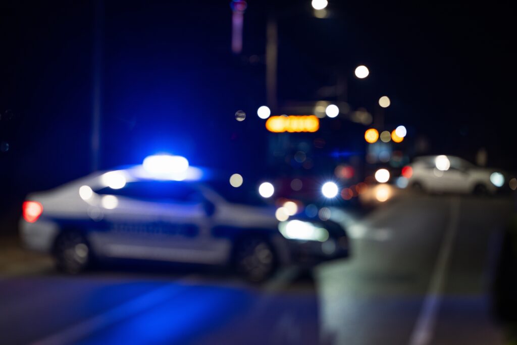 A blurred photo of a police car pulled crossways in the road, blocking traffic. Blue light on.