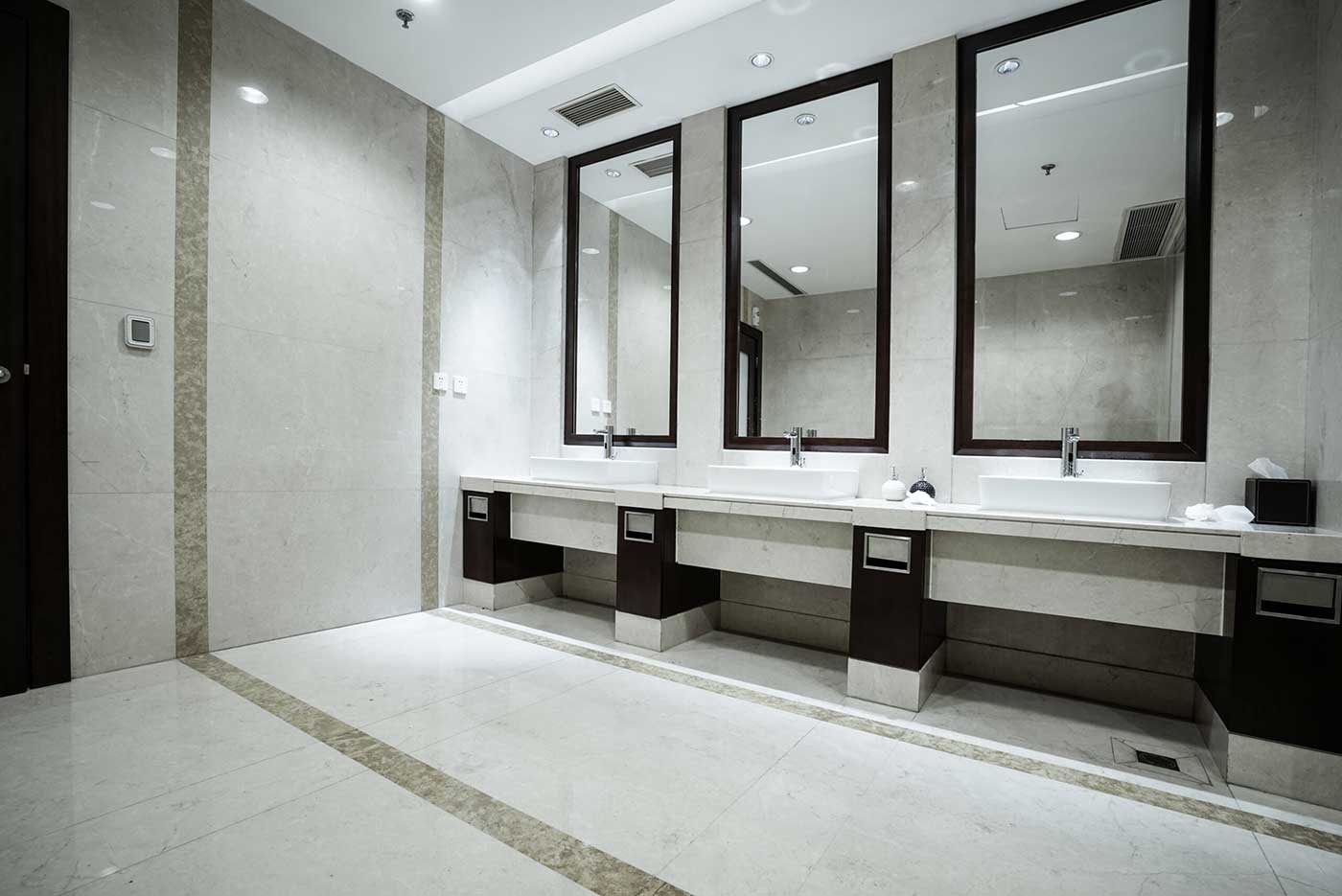 Modern public restroom with gleaming white tile floors. Three sinks below mirrors.