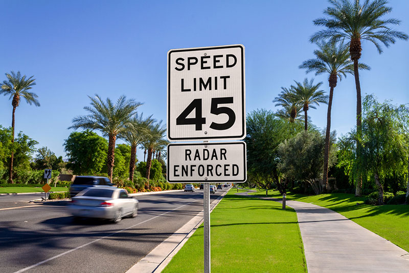 A speed limit sign along a California street lined with palm trees. The sign reads Speed Limit 45 Radar Enforced